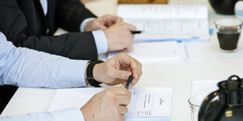 Et møde i Arbejdsmiljørådet, ser armene på en person, som sidder med en kuglepen i hænderne.