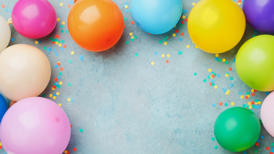 Balloner i forskellige farver ligger på en grå baggrund med konfetti